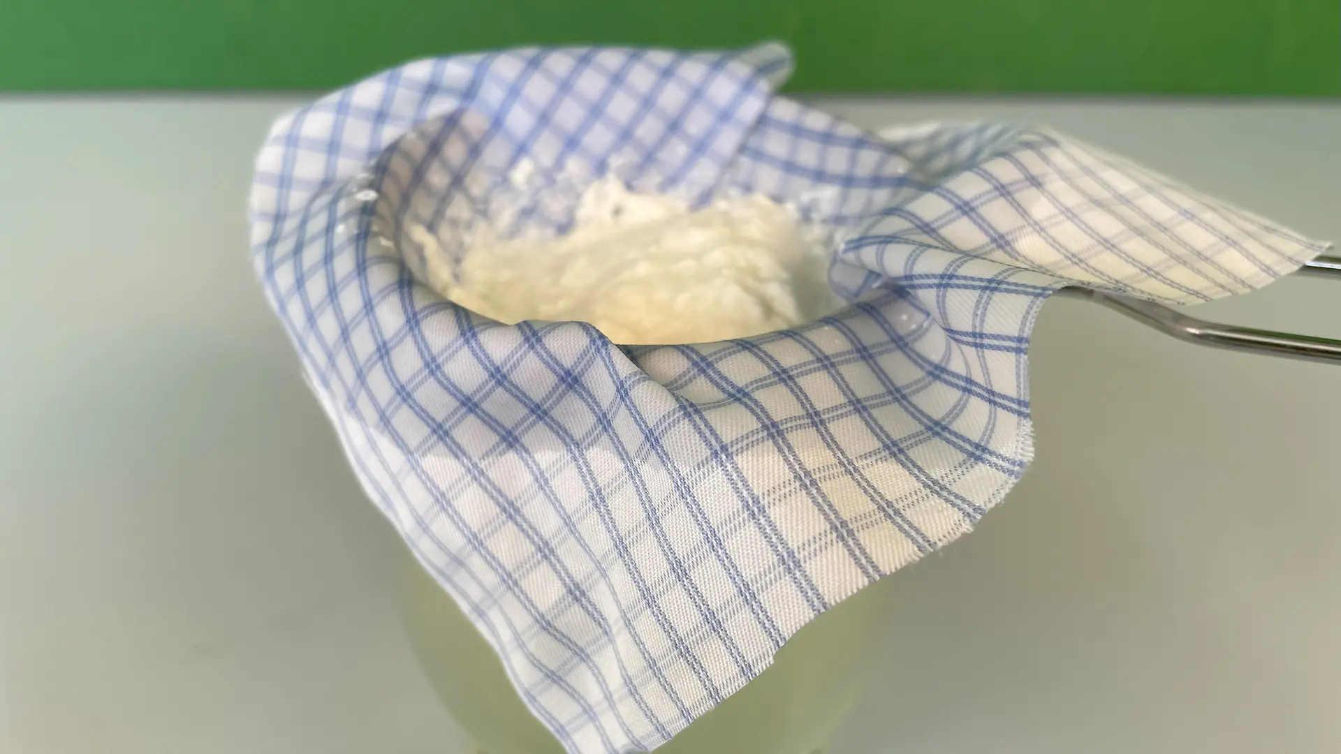 Glass on which a sieve with a piece of cloth is lying. The curdled milk can be seen on the piece of fabric.