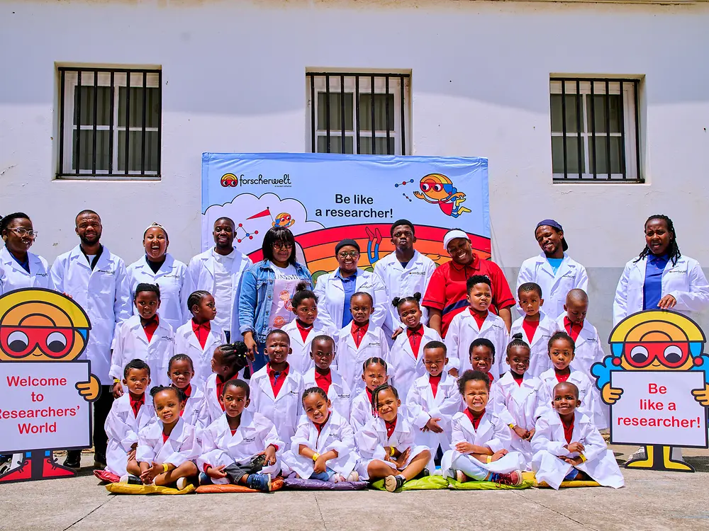 A large group of children and adults wearing lab coats at a Researchers’ World event.